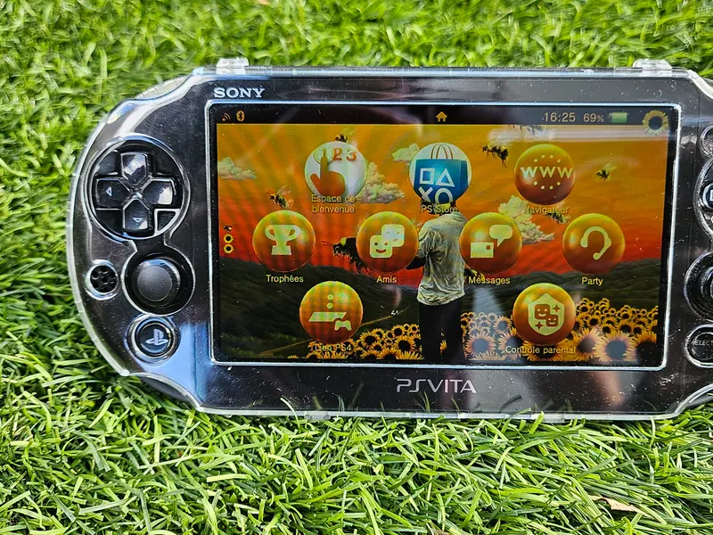PS Vita 2000 noire en coque transparente, écran LCD allumé sur un thème Tournesols